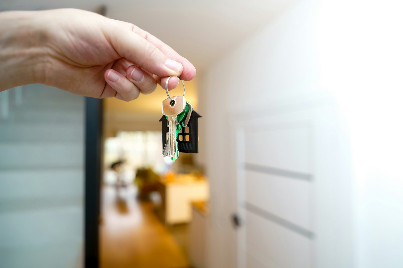 Hand hält den Schlüssel zur neuen Wohnung vor der Eingangstür